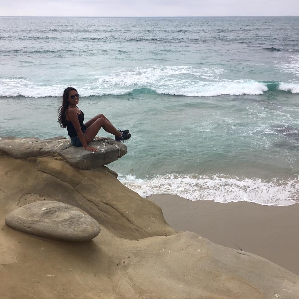 me sitting joyfully on a large rock by the beach, a symbol of grounding, strength, and freedom. It represents the calm and clarity I’ve gained through meditation and ThetaHealing. The ocean reflects the vastness of the soul, while the rock anchors the journey — showing what’s possible when we heal from within.